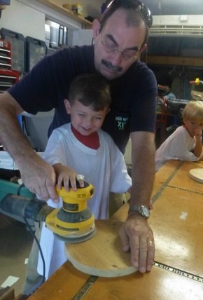 grandfather helping grandson use an electric sander - camp cece