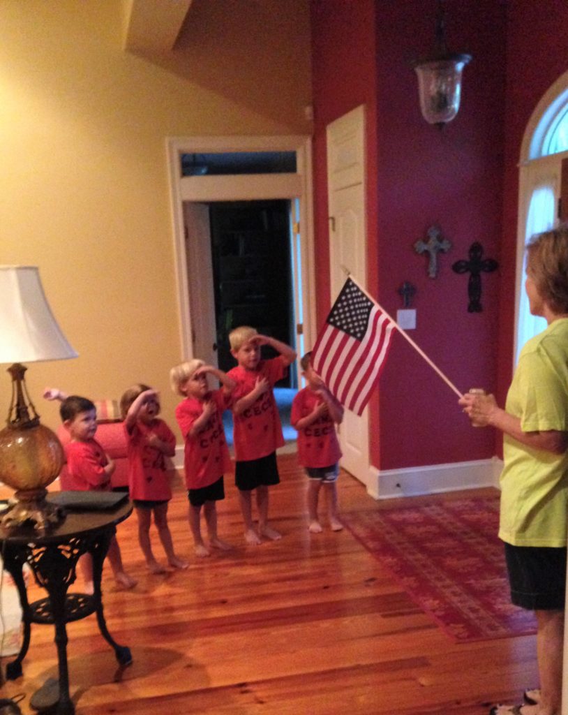 kids standing with their hands over their hearts facing an American flag.
