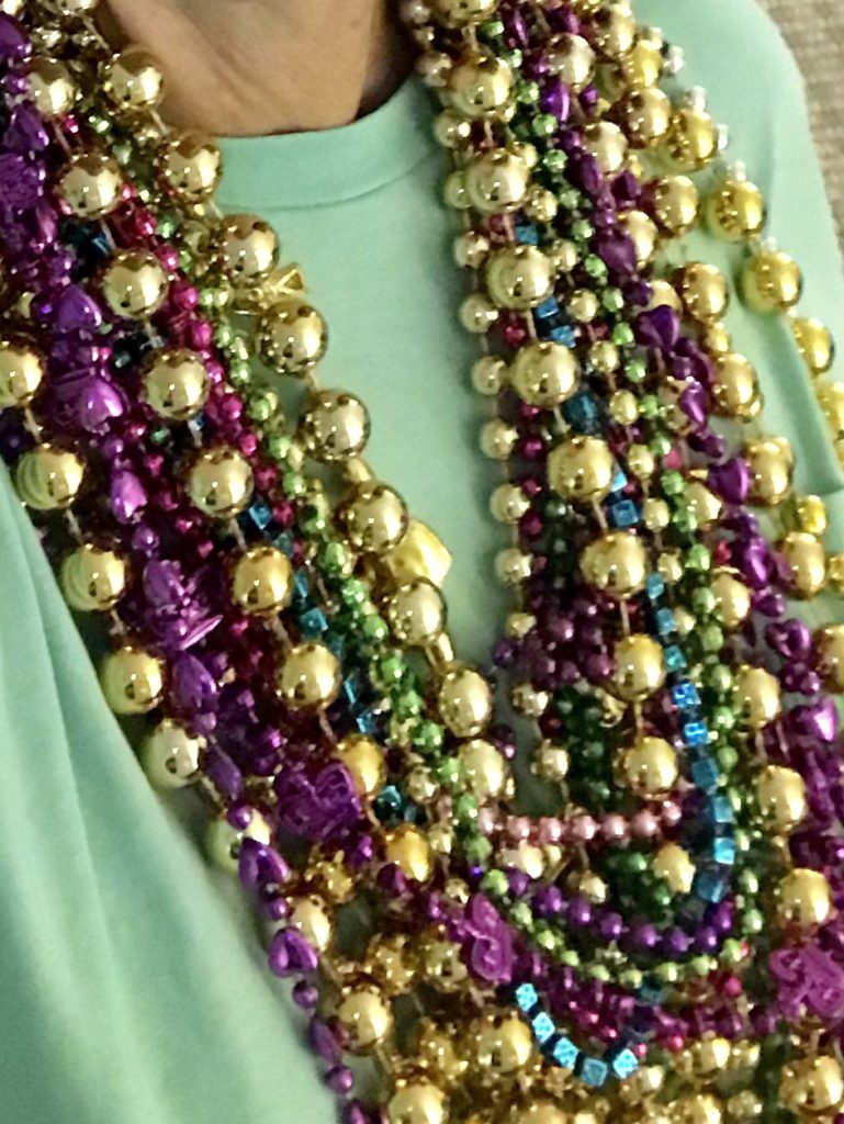 a large number of mardi gras beads around a woman's neck